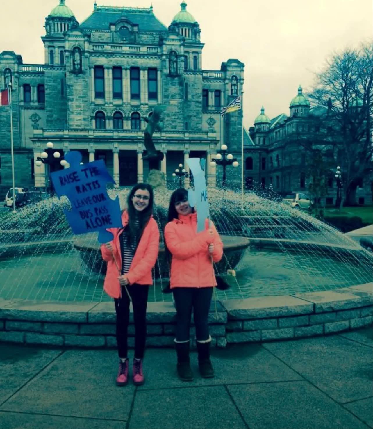 Two people holding advocacy signs outside the British Columbia Parliament Buildings